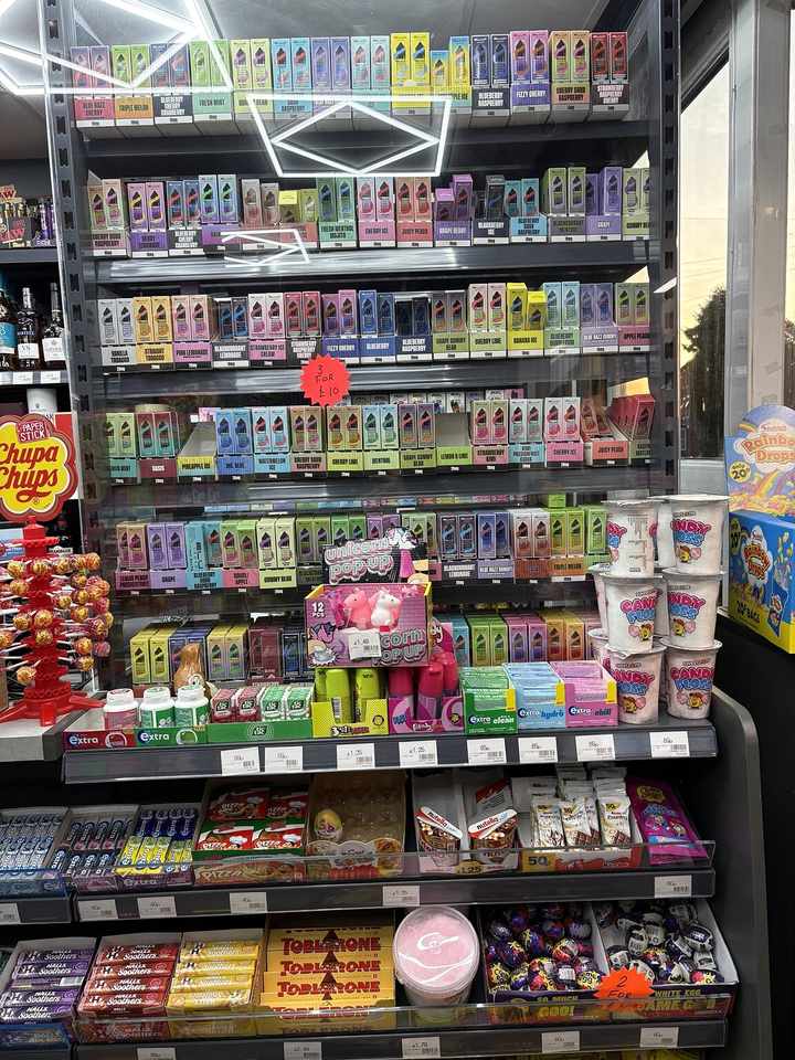 Age-restricted vape products displayed behind the counter, alongside sweets and confectionery, at C&K Local Store.